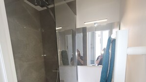 Een moderne badkamer met een douchecabine van glas, een wit wastafelmeubel met een spiegel erboven en een handdoek aan een rek.