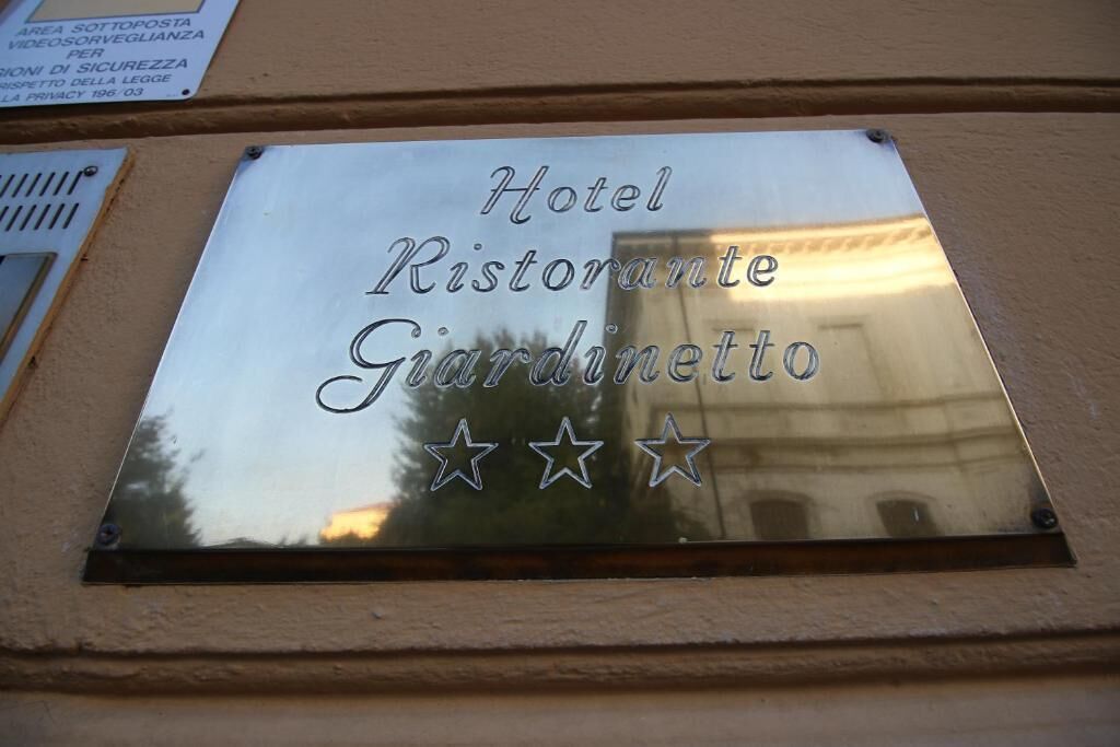 Una placa metálica con el texto 'Hotel Ristorante Giardinetto' y tres estrellas.