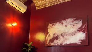 Una habitación con techo de ladrillo, un sofá blanco con cojines, aire acondicionado instalado en la pared y un cuadro abstracto grande.