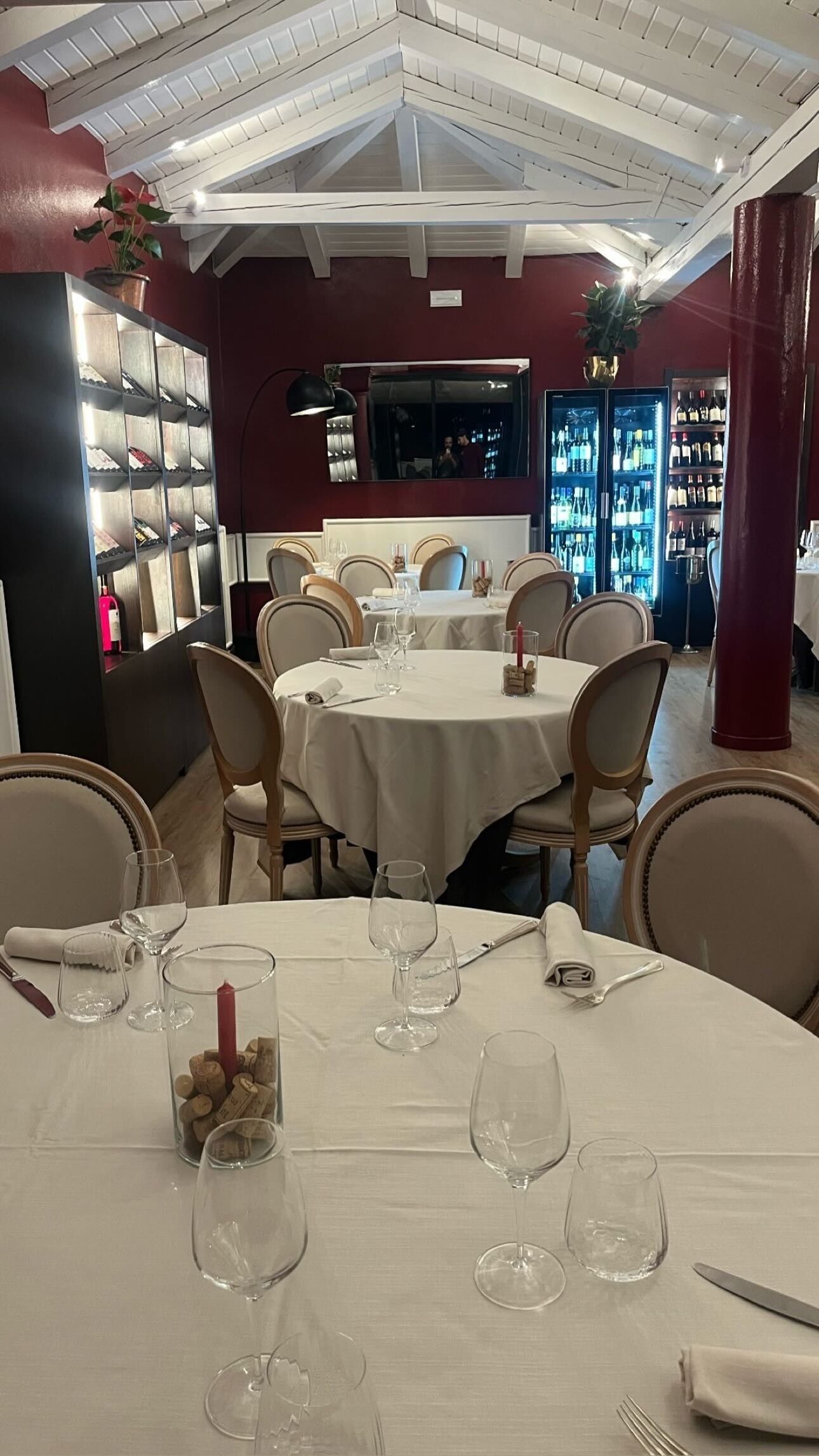 Un restaurant avec des tables rondes, des chaises, des verres à vin et une bouteille de vin posée sur la table.