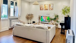 Un salon moderne avec un canapé, un téléviseur à écran plat, un luminaire au plafond et une fenêtre avec des rideaux.
