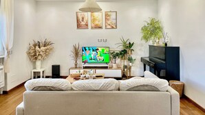Un salon moderne avec un canapé, un téléviseur, un piano et des plantes décoratives.