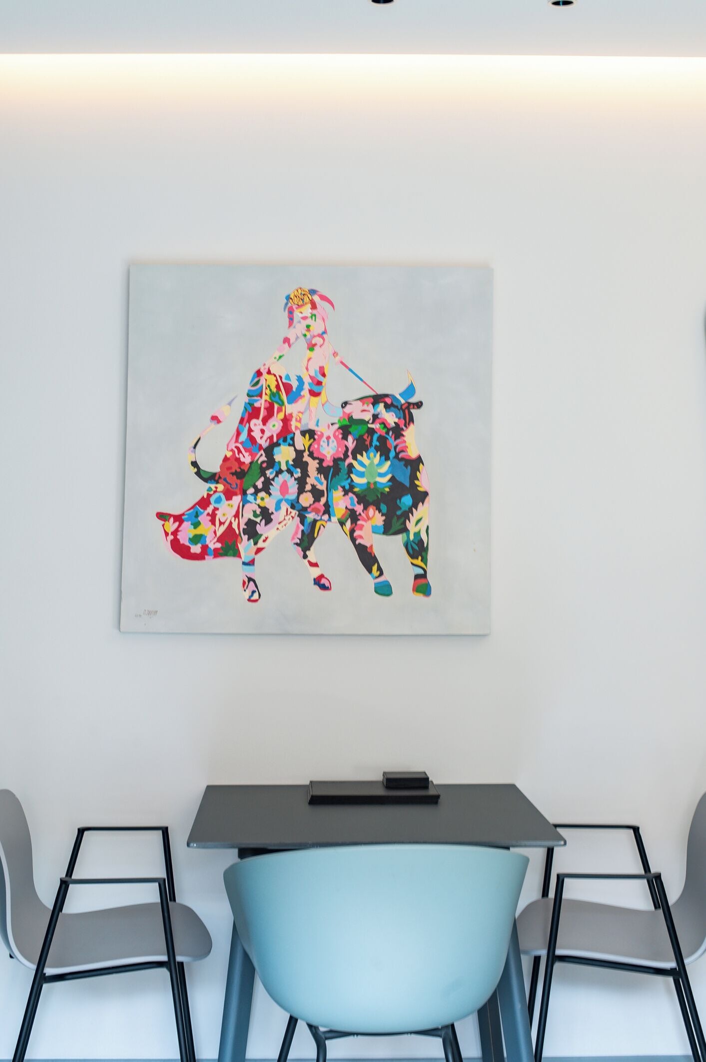 A modern room with a light blue chair, a table, and a colorful abstract painting on the wall.