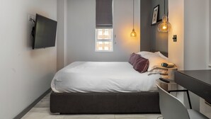 A modern bedroom with a bed, bedside table, lamp, and a TV mounted on the wall. - Nell Gwynn House Apartments & Rooms (London)