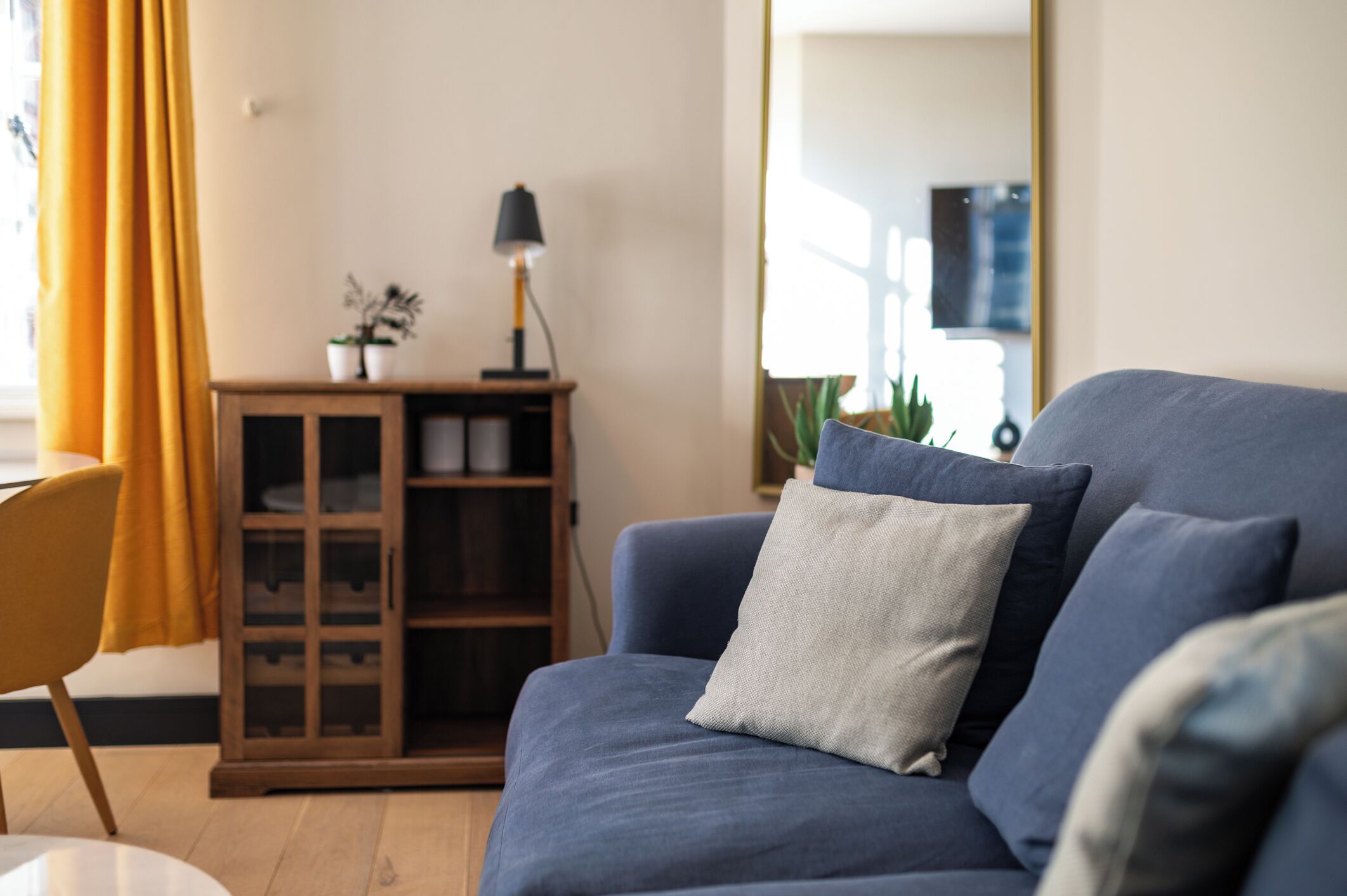 Un salon avec un canapé bleu, un meuble en bois, une lampe et un miroir.