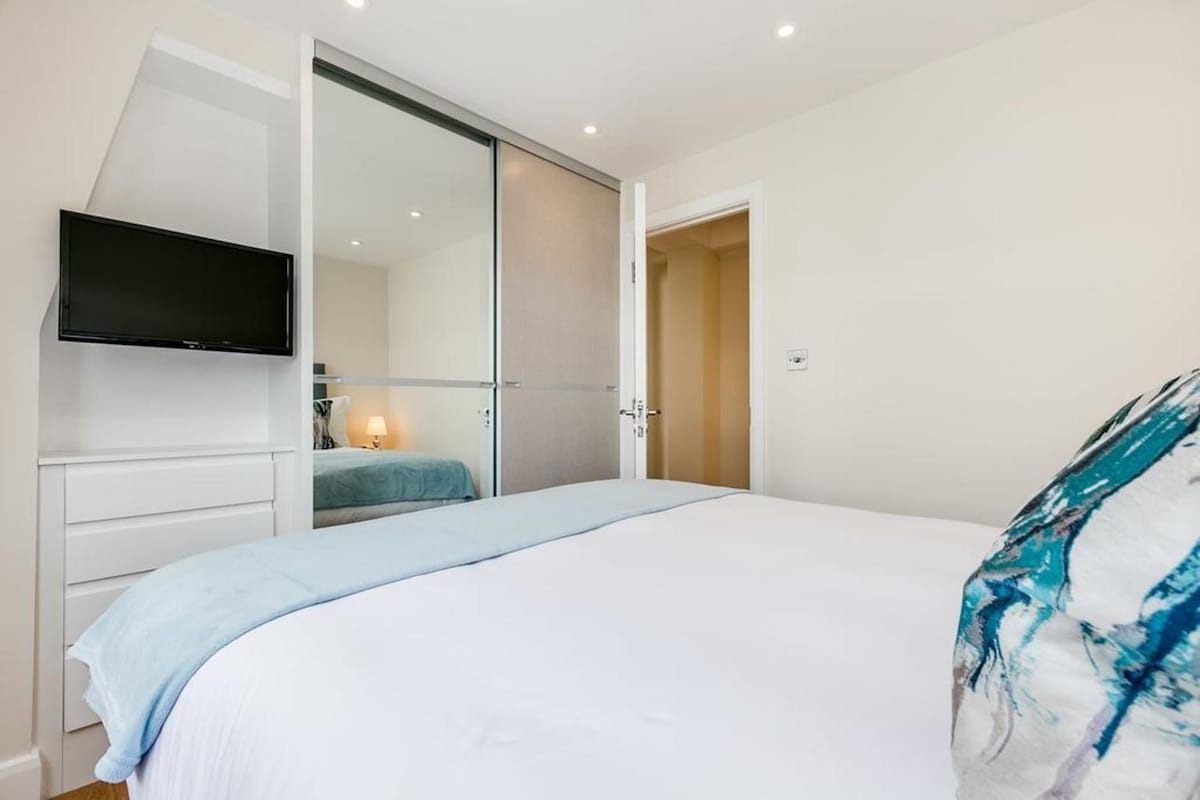 A bedroom with a bed, a TV mounted on the wall, a sliding door closet, and a bedside lamp.