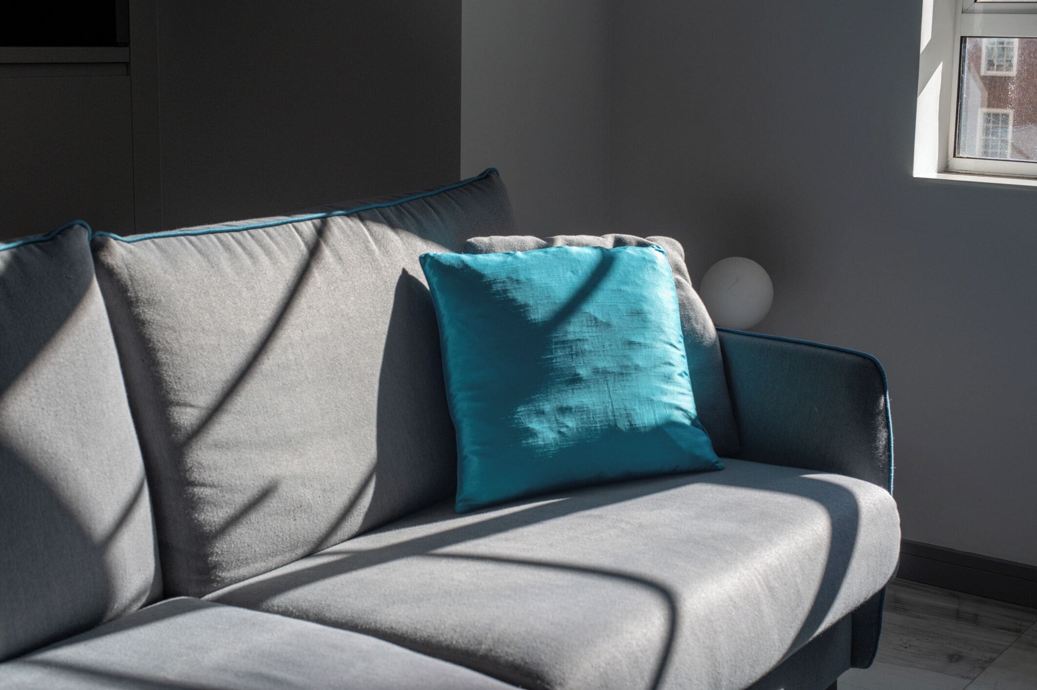 A grey sofa with a teal cushion and a round white object on it.
