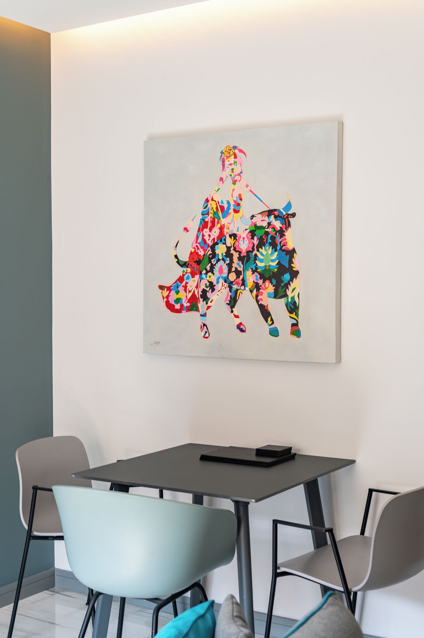 Een moderne kamer met een eettafel, twee stoelen en een kleurrijk abstract schilderij aan de muur.