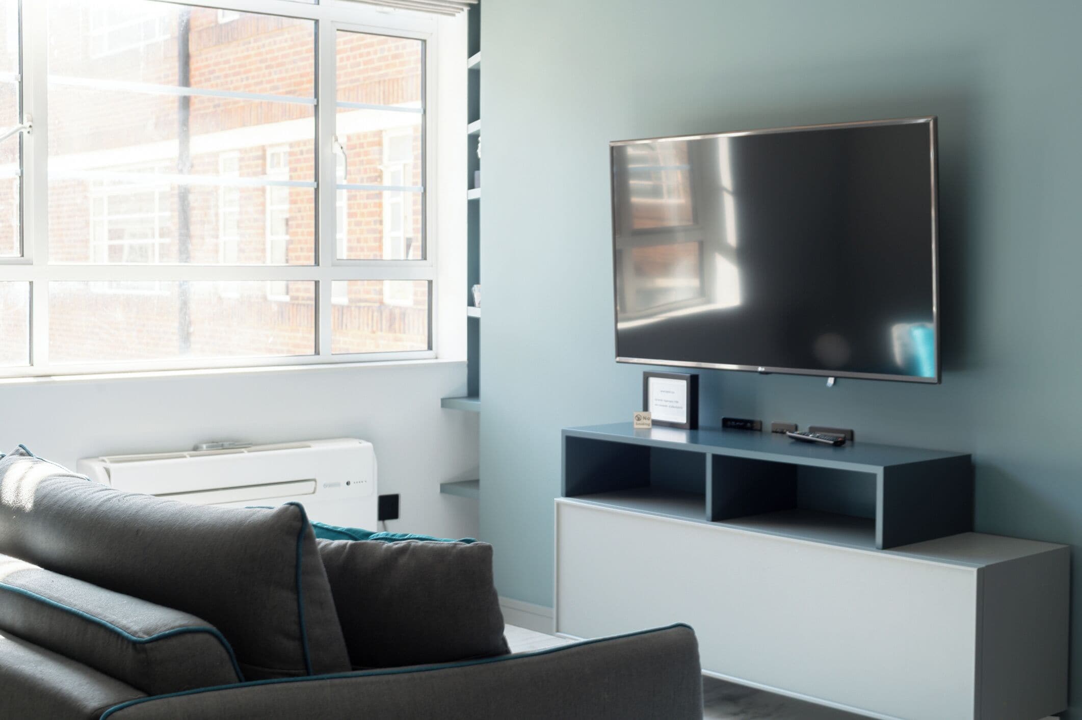Un soggiorno moderno con un'ampia televisione a schermo piatto montata a parete, un divano grigio con finiture blu e un termosifone bianco.