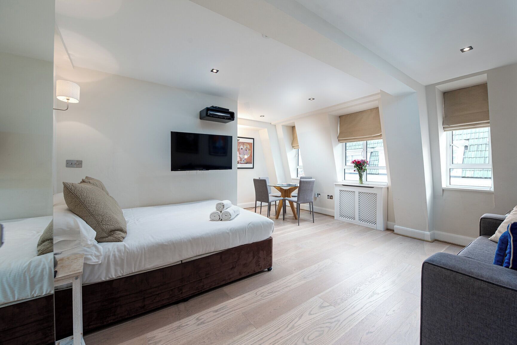 Een moderne, goed verlichte kamer met een bed, een bureau en een stoel, met een flatscreen-tv, een radiator en een raam met uitzicht.