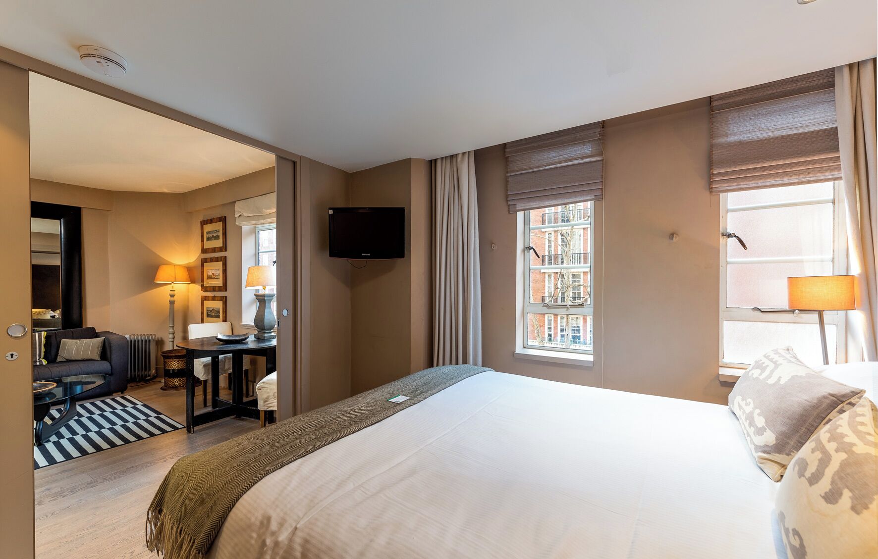 A hotel room with a bed, a television, a desk with a chair, a lamp, and a window with curtains.