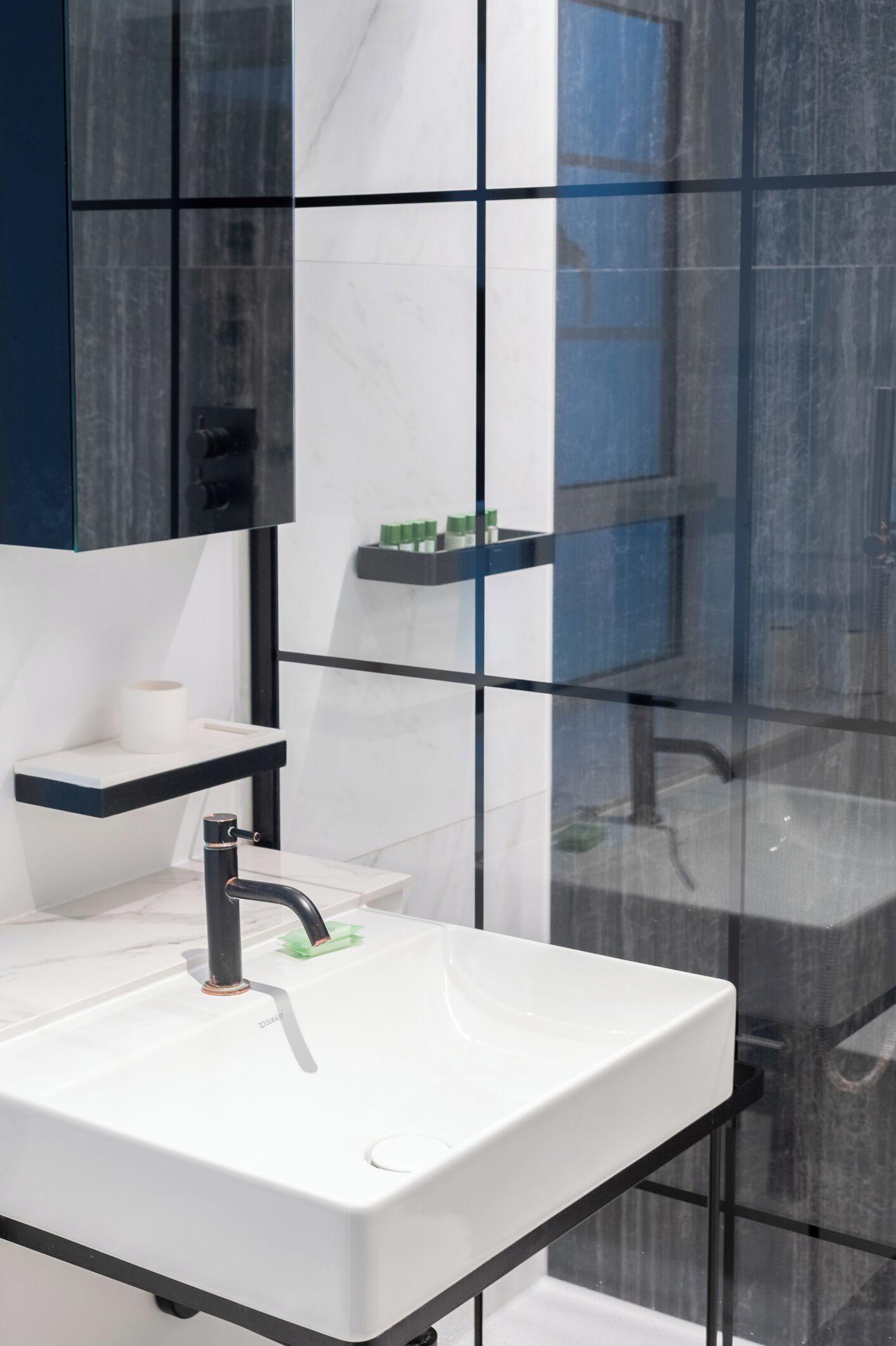 A modern bathroom with a white sink, black faucet, and a glass shower enclosure.
