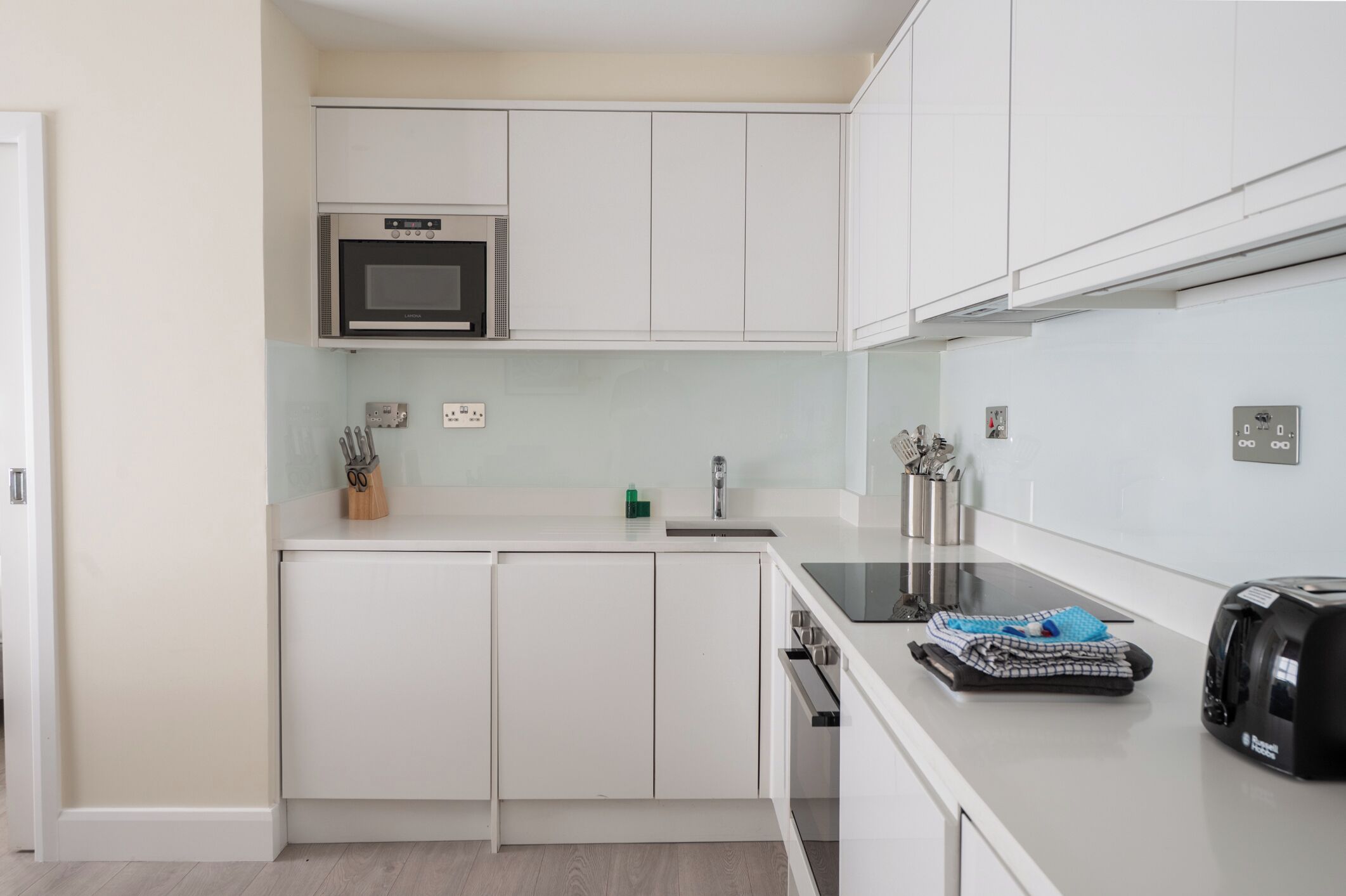 Une cuisine compacte avec des meubles blancs, un four à micro-ondes encastré, un évier et un grille-pain.