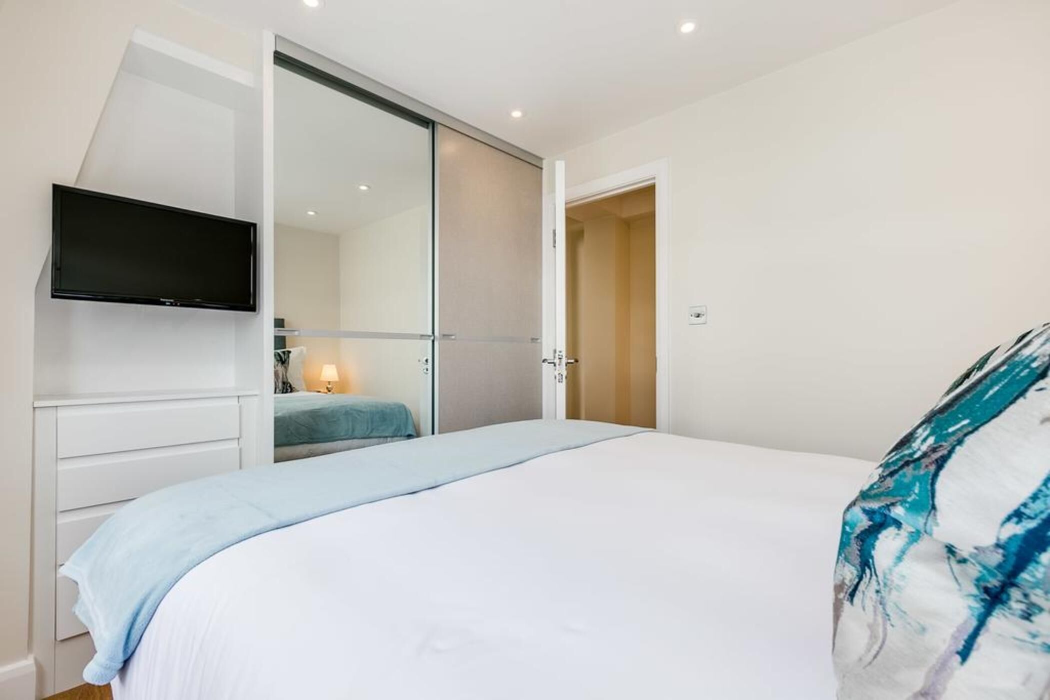A bedroom with a bed, a TV mounted on the wall, a sliding door closet, and a bedside lamp.