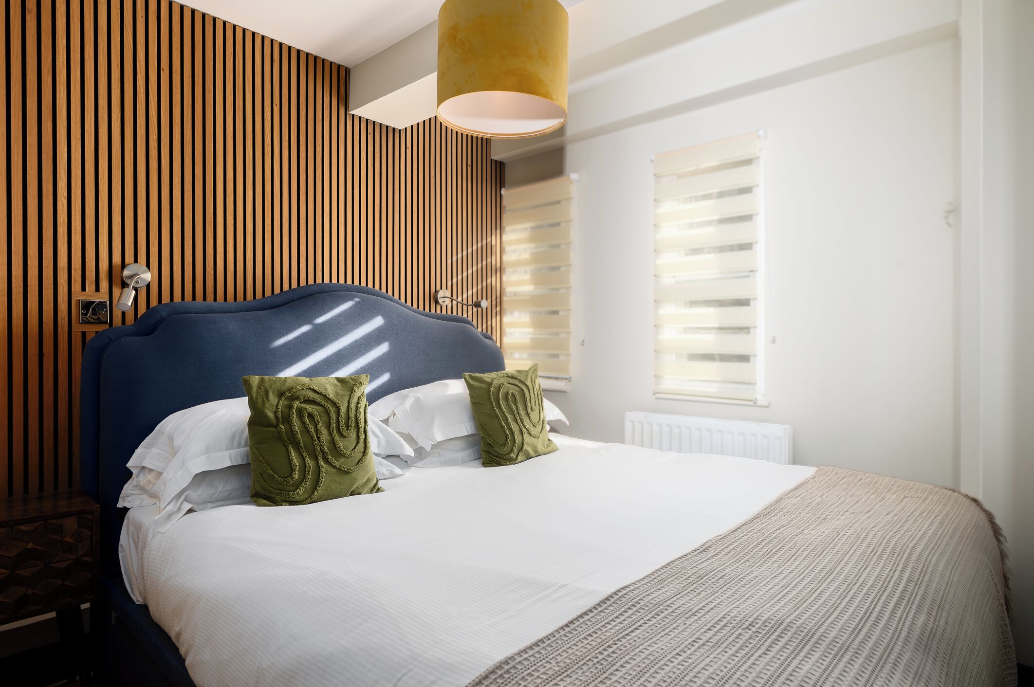 A hotel room with a large bed, wooden panel walls, a ceiling light, and a window with blinds.