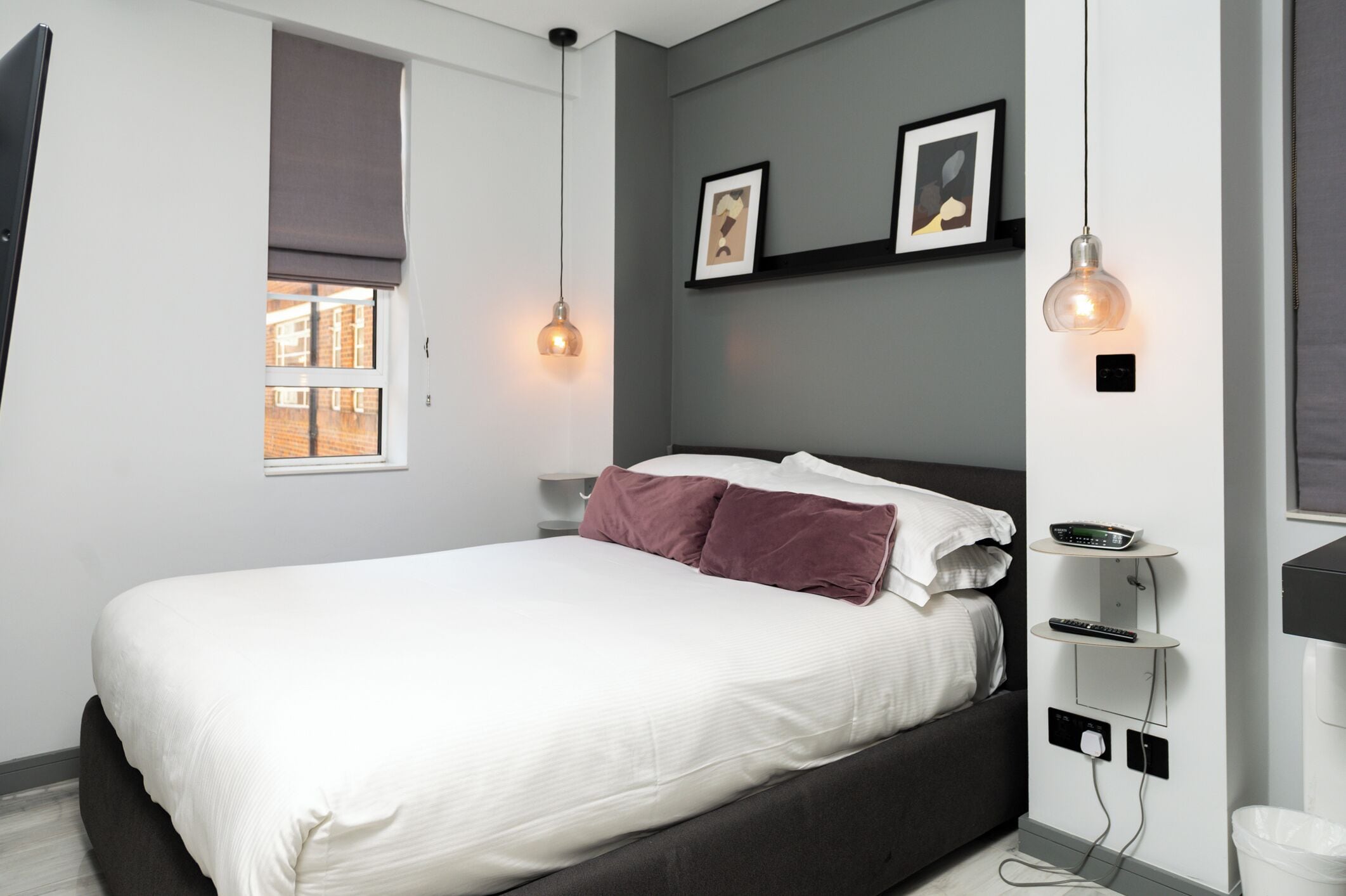A modern bedroom with a bed, bedside tables, a window with blinds, and wall-mounted light fixtures.