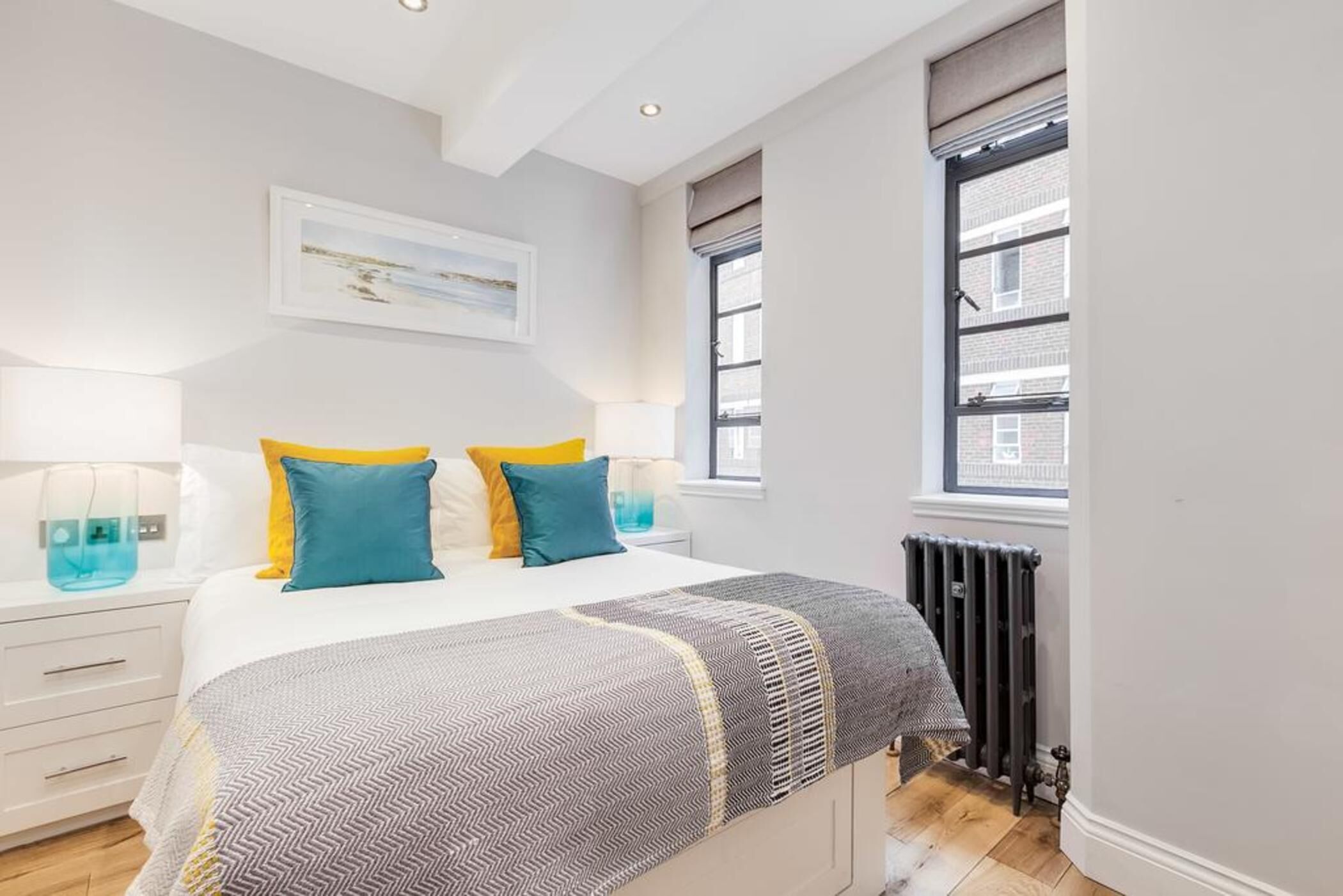 A bedroom with a bed, bedside tables, a radiator, and a window with a view.