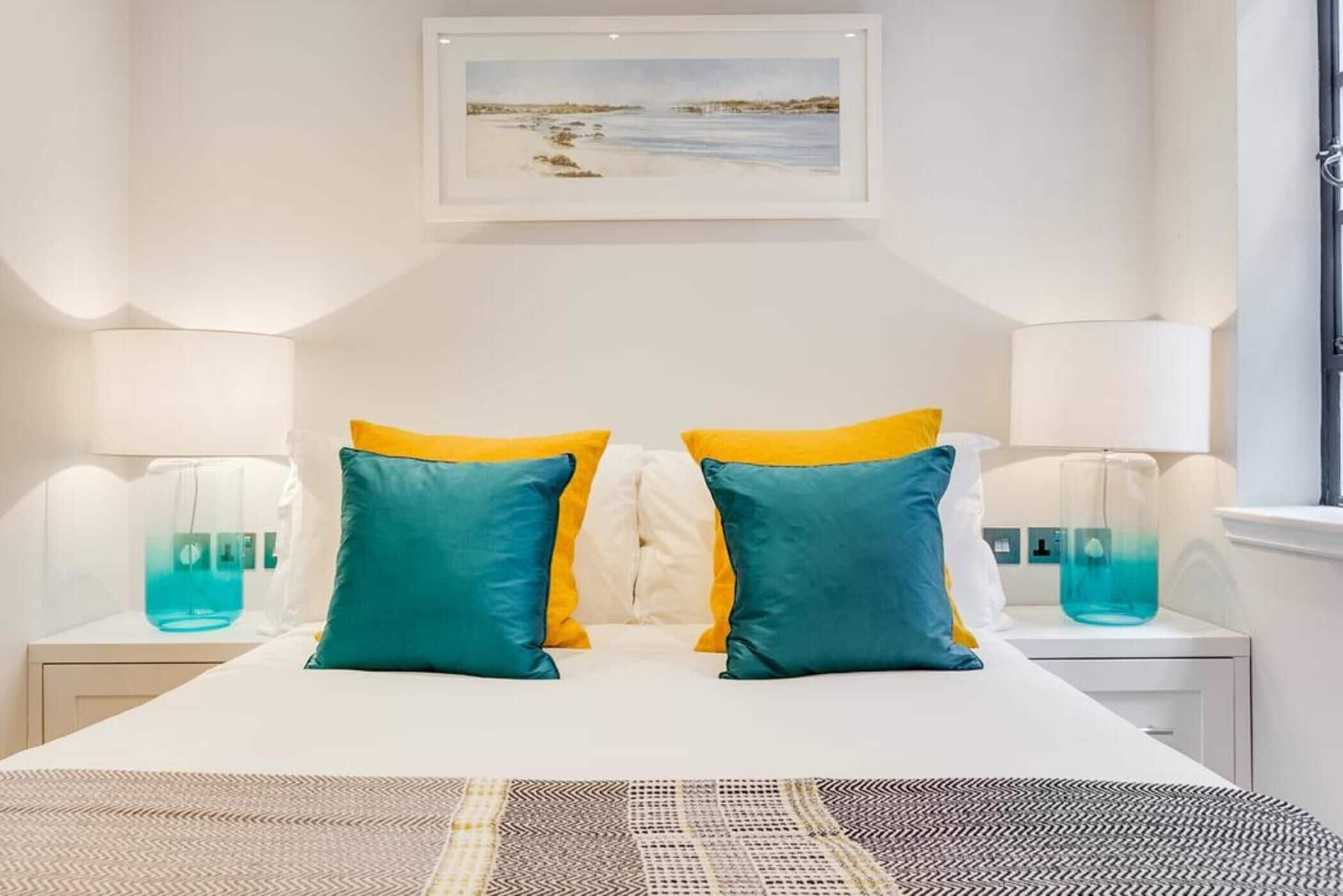 A hotel room with a bed, two bedside tables with lamps, a framed picture on the wall, and a window.