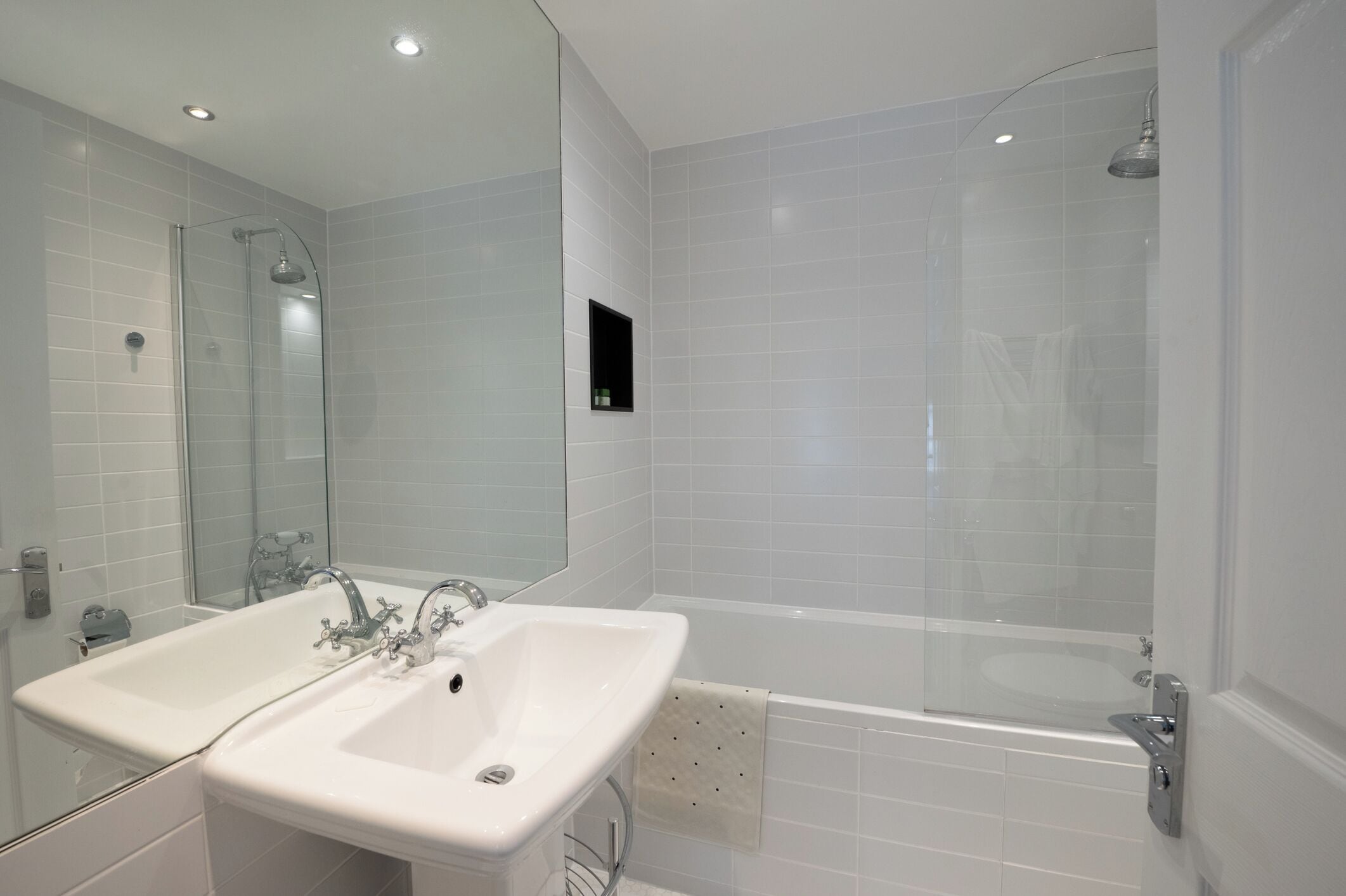 A modern bathroom with a double sink, a glass-enclosed shower, and a large mirror.