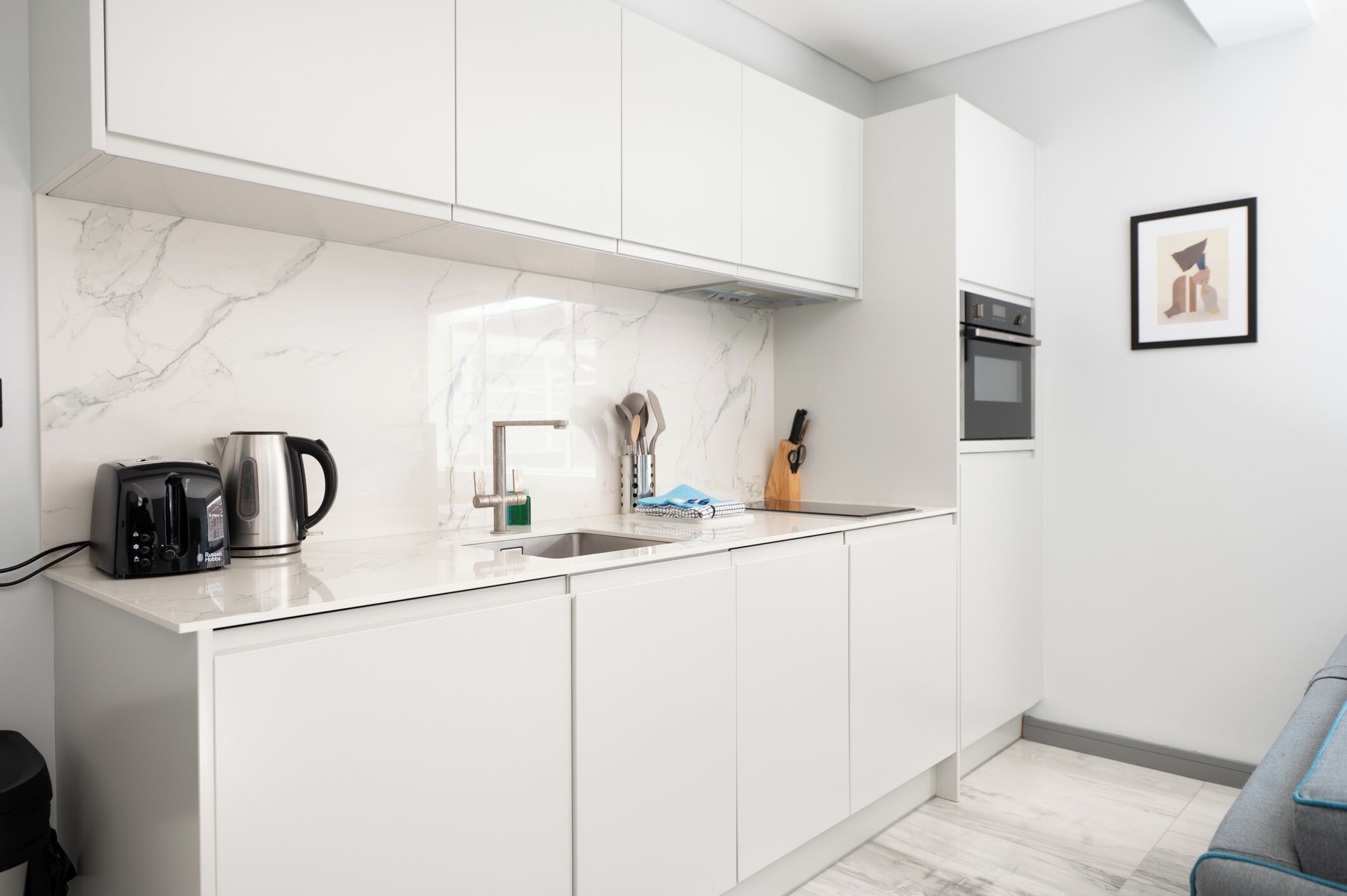 A modern kitchen with white cabinets, a marble backsplash, a built-in oven, and a coffee maker.