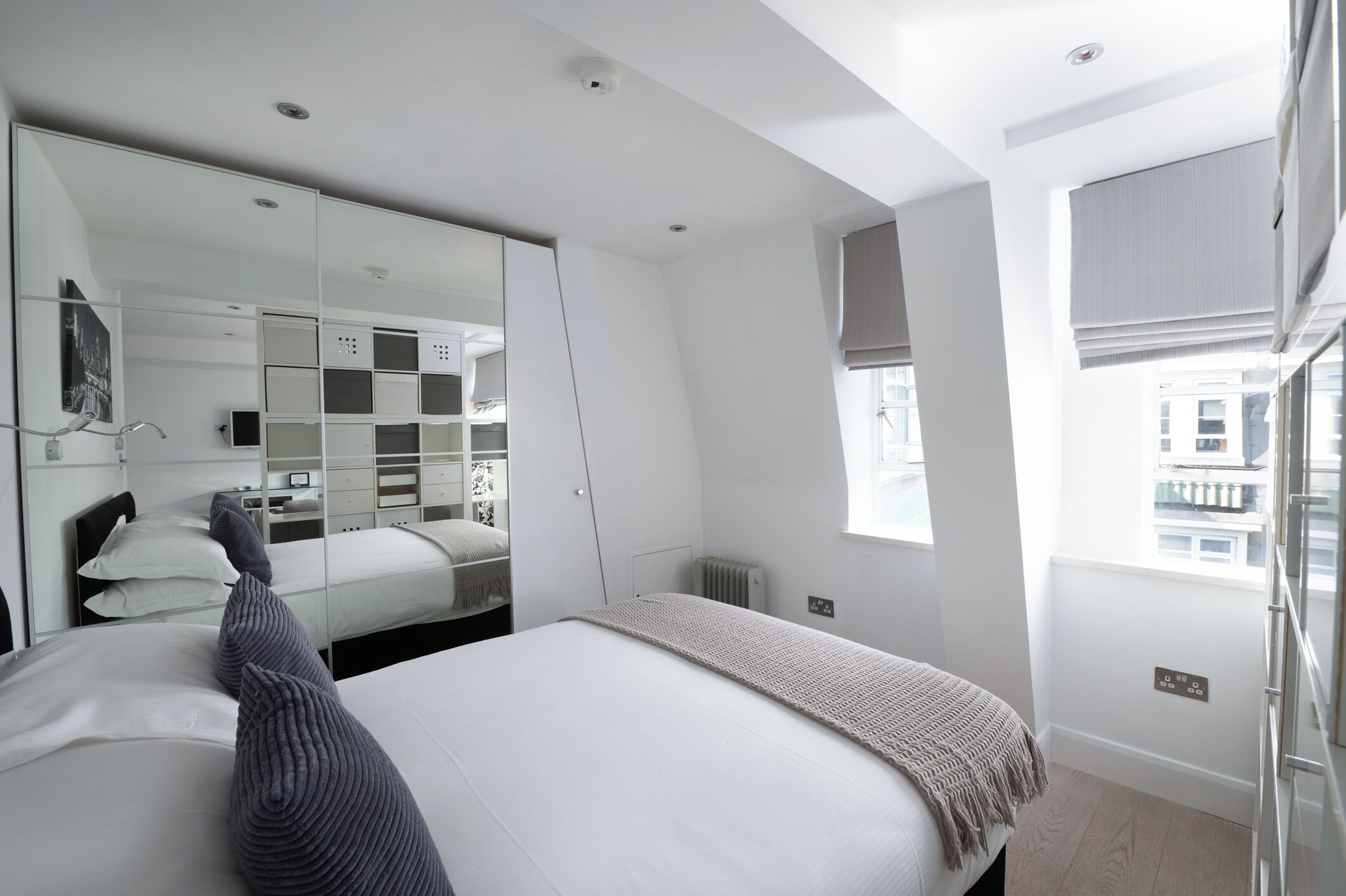 Una habitación de hotel moderna con una cama grande, un espejo, un armario y una ventana con vistas.