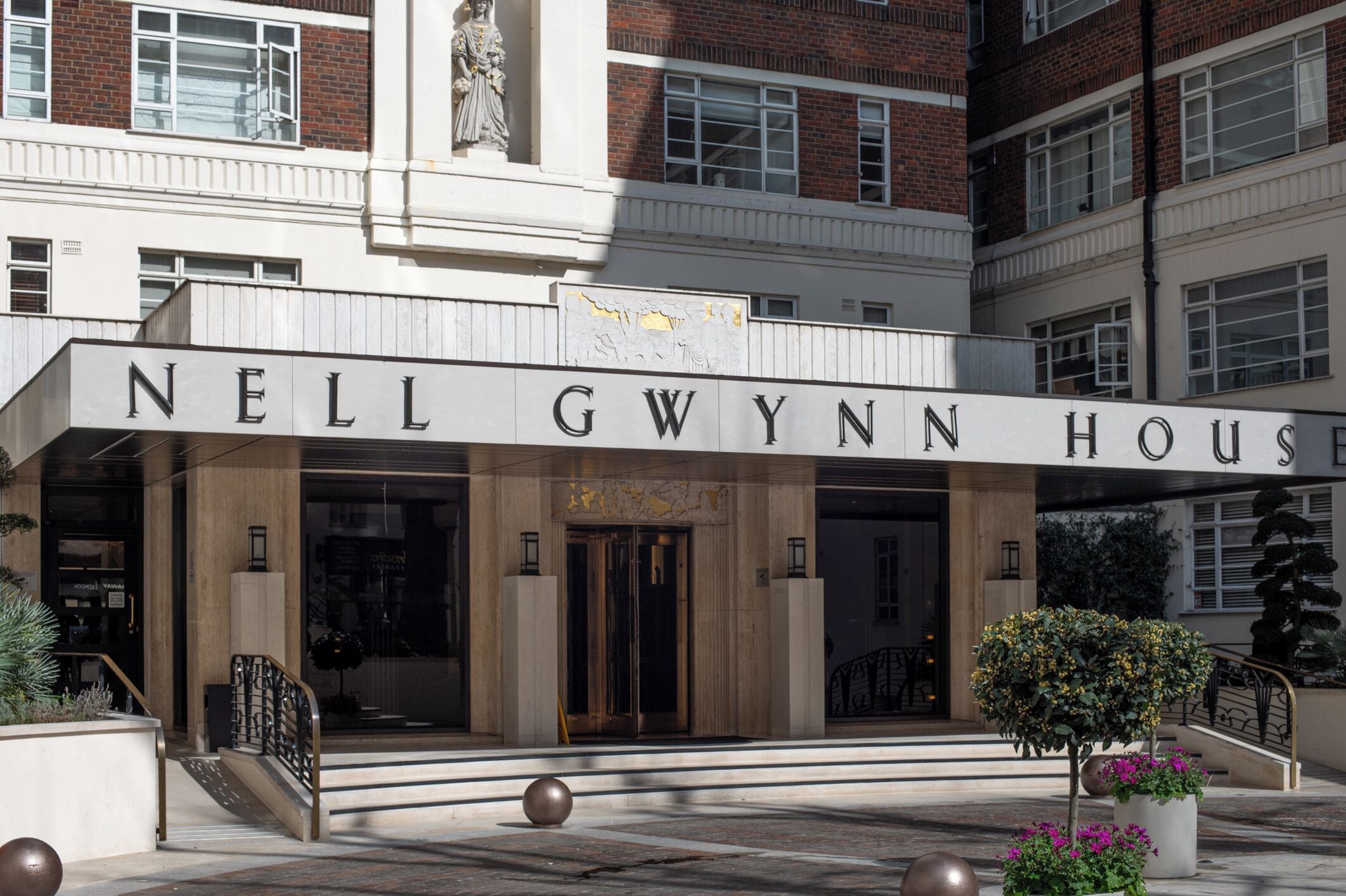 A hotel entrance with a name sign, a statue, and a staircase leading to the door.