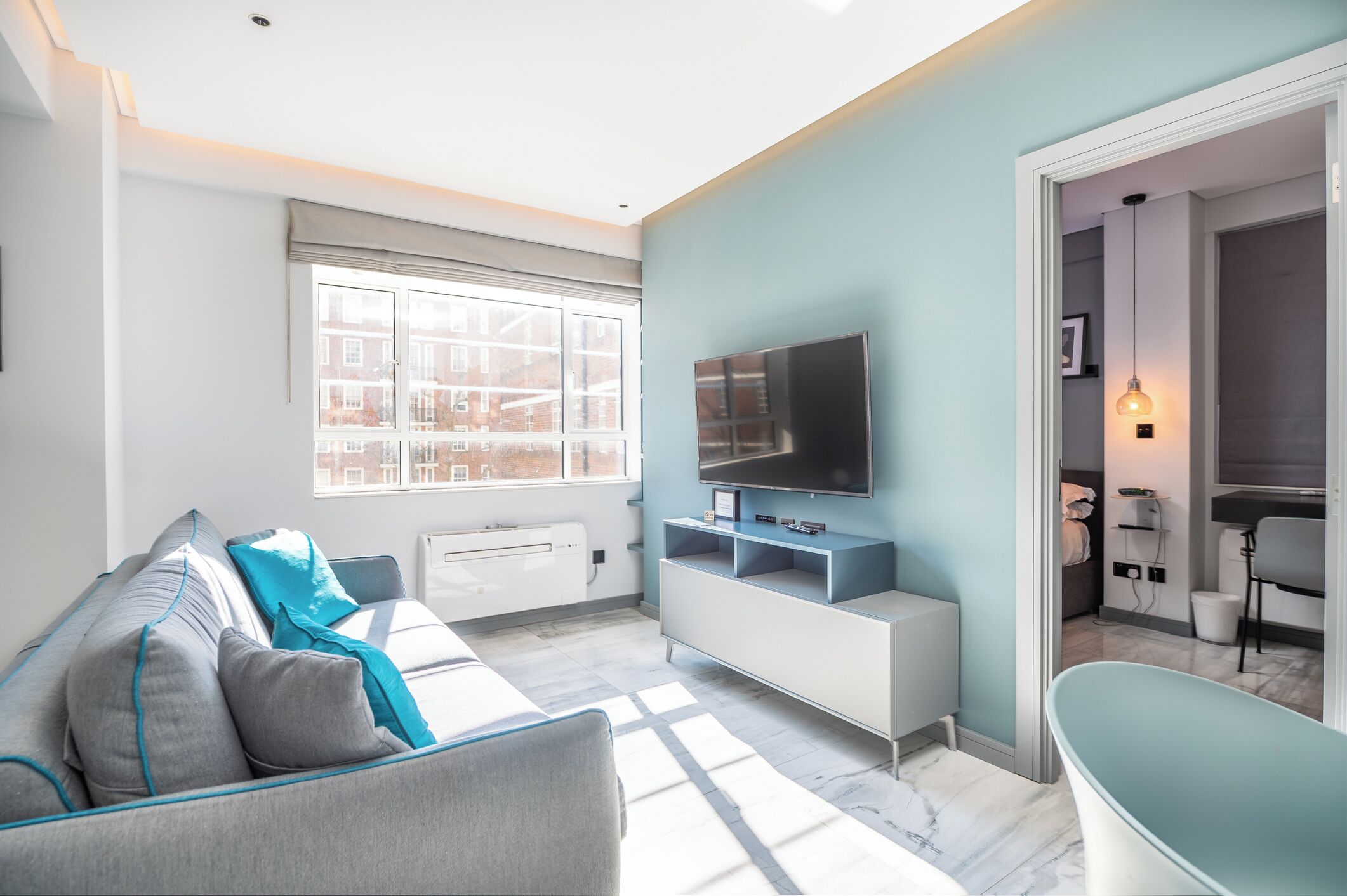 Ein modernes Wohnzimmer mit Sofa, Fernseher und Blick ins Freie.