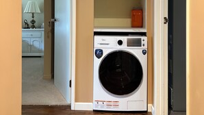 A laundry room with a front-loading washer and dryer, wooden flooring, and a white door leading to another room.