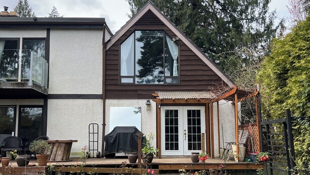 A two-story house with a deck, a garage, and a garden with various plants and flowers.