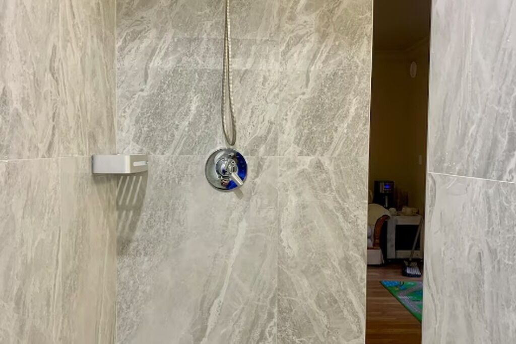 Ein Badezimmer mit Marmorwänden, einer Duschbrause und einer sichtbaren Tür zu einem anderen Raum.