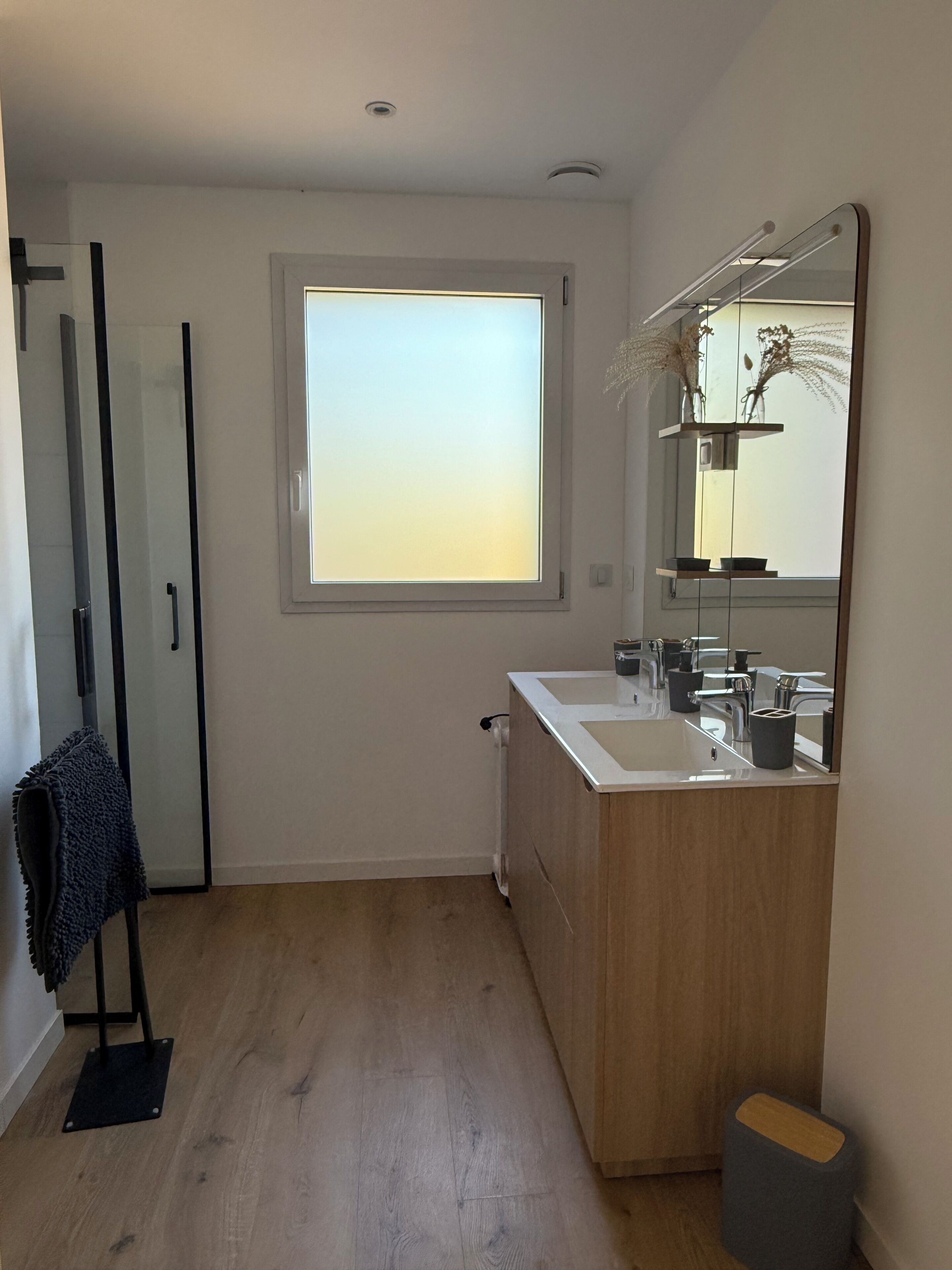 Un baño con ventana, espejo, lavabo y toallero.