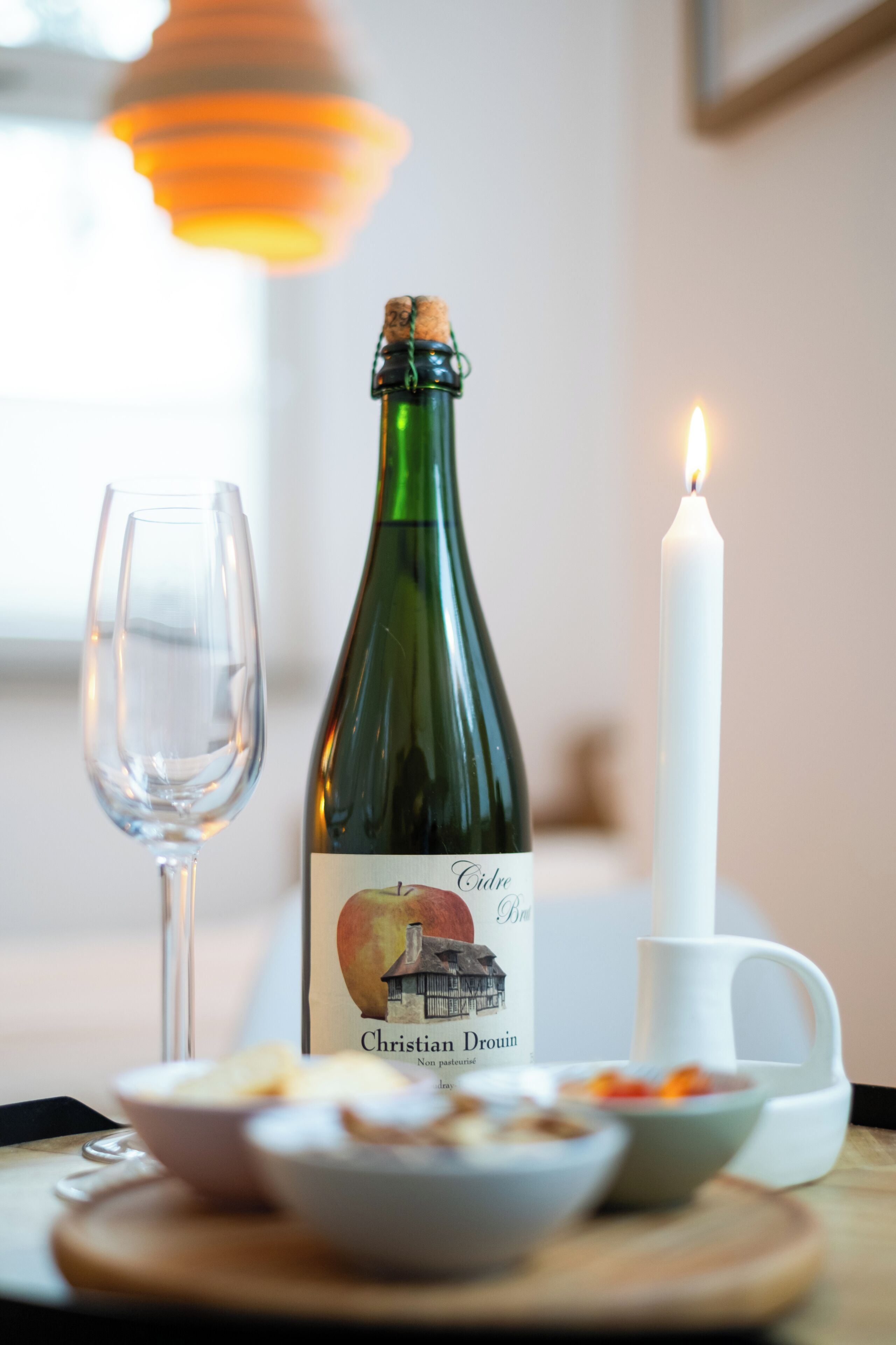 A bottle of wine, a glass, a candle, and bowls of food on a table.