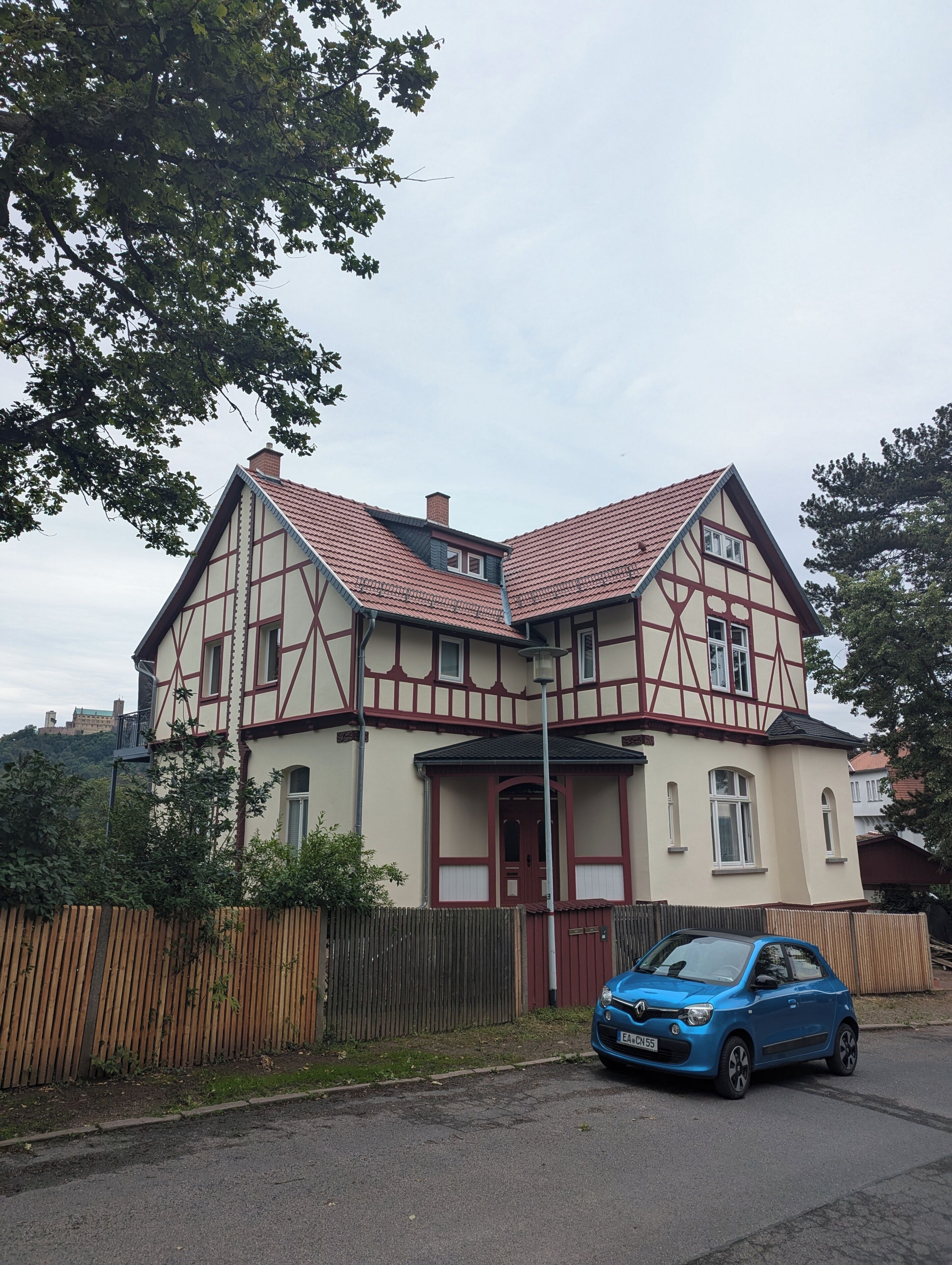 A two-story house with a steeply pitched roof, a visible chimney, and a small balcony.