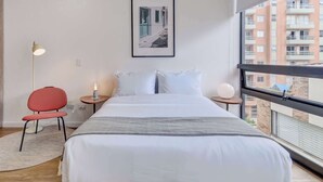 Et moderne hotelværelse med en stor seng, en rød stol, et natbord med en lampe og et billede i ramme på væggen.