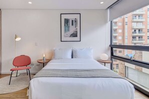 A modern hotel room with a large bed, a red chair, a bedside table with a lamp, and a framed picture on the wall. - w* | Loft Haven in the Heart of Bogotá (Bogotá)