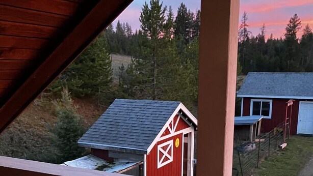 Holzgeländer eines Balkons mit Blick auf eine ländliche Landschaft, mit einem roten Bauernhaus und einem blauen Haus.