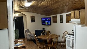 Eine kompakte Küche mit Holzausstattung, einem Esstisch mit Stühlen, einem an der Wand befestigten Fernseher und einem Kühlschrank.