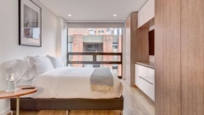 A modern bedroom with a bed, bedside table, and a large window with a view of a brick building.