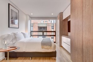 A modern bedroom with a bed, bedside table, and a large window with a view of a brick building. - w* | Signature Loft in the Heart of Bogotá (Bogotá)