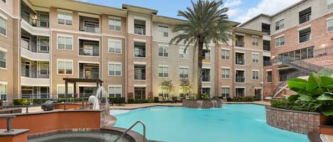 A multi-story residential building with a swimming pool, a hot tub, and a palm tree.
