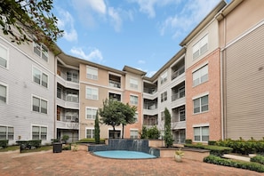 A courtyard with a swimming pool, surrounded by multi-story buildings with balconies and a clear sky.
