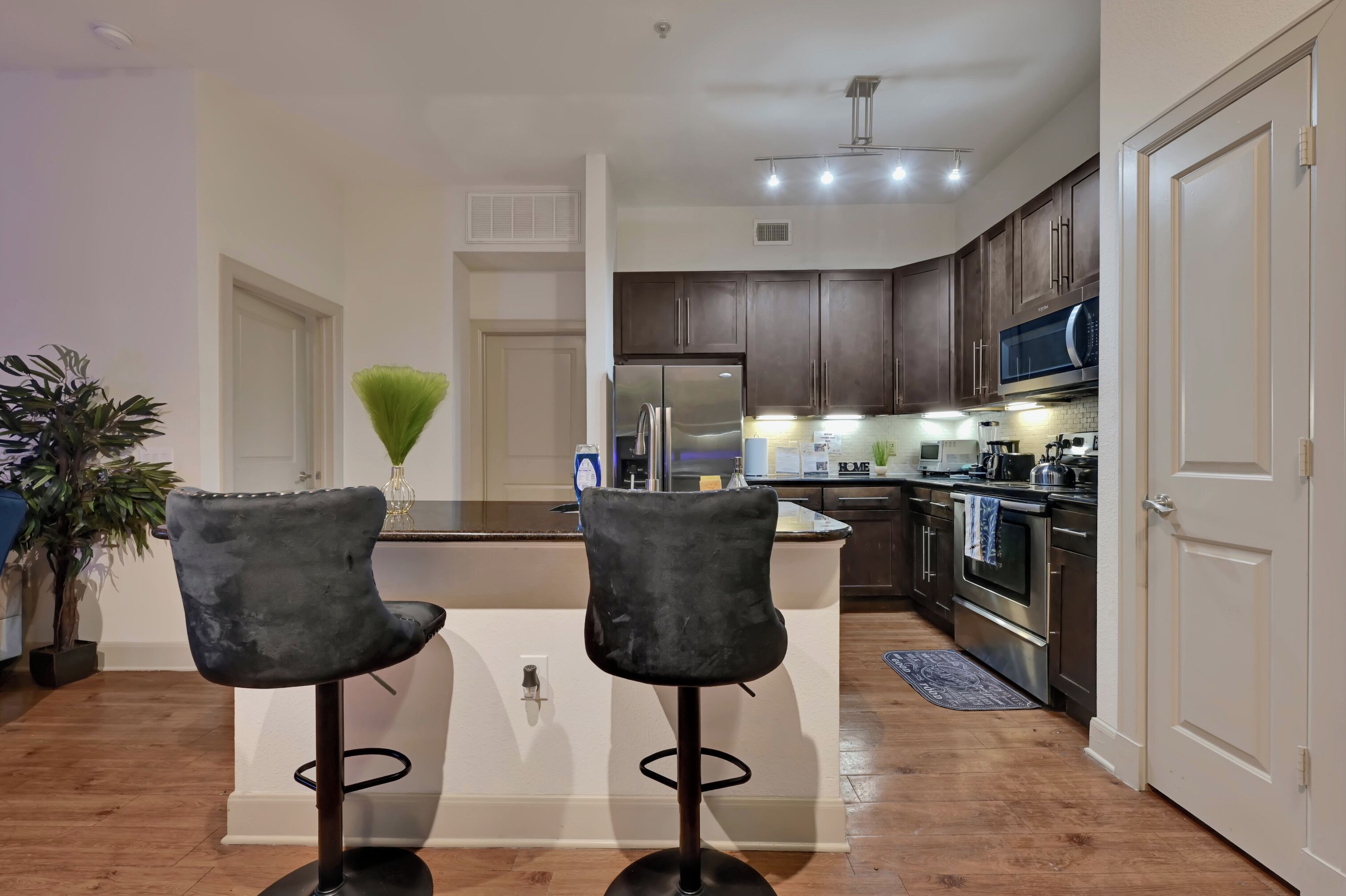 A modern kitchen with dark cabinets, stainless steel appliances, and a central island with two bar stools.