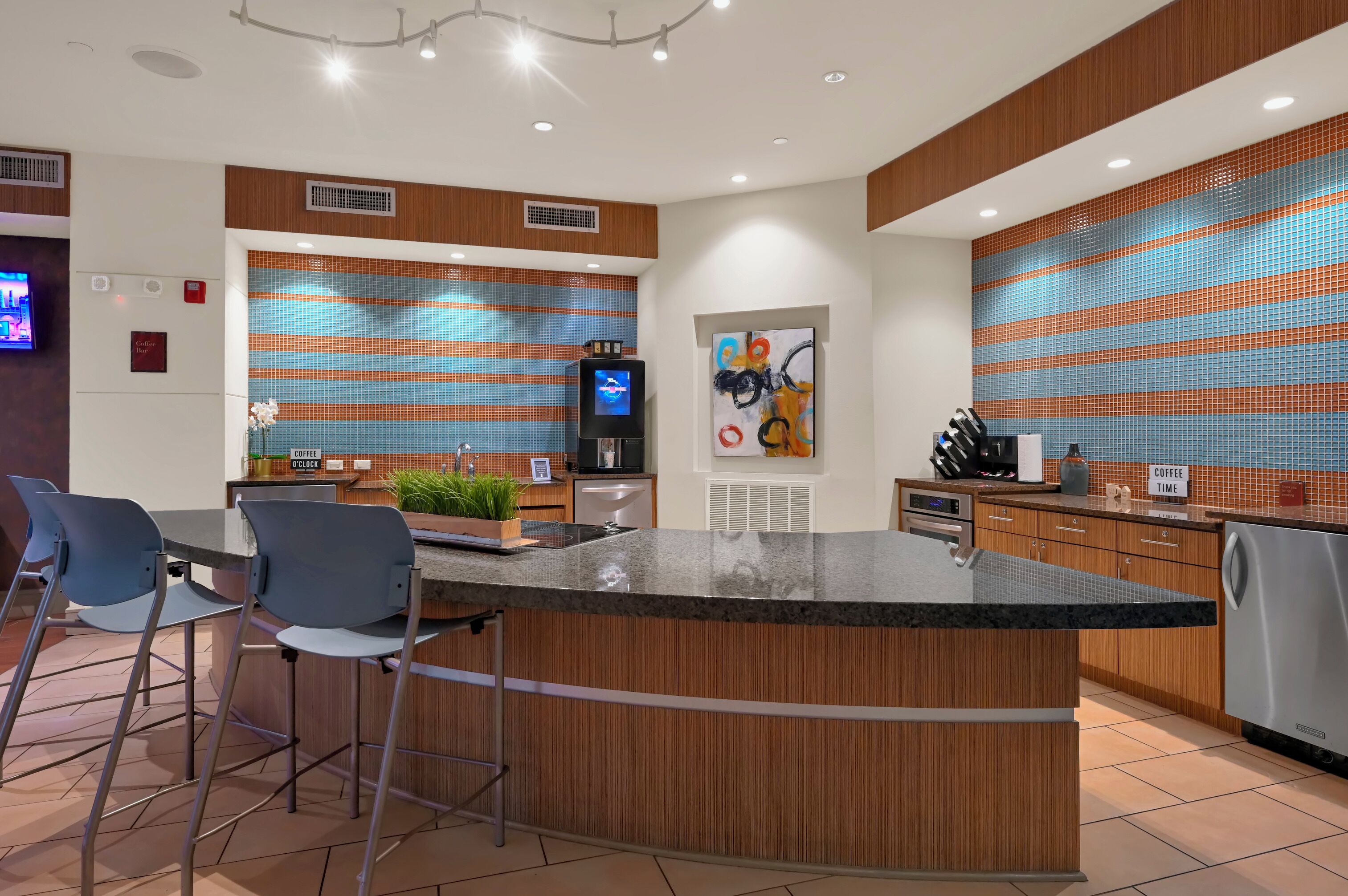 A modern kitchen with a central island, bar stools, a coffee station, and a TV.