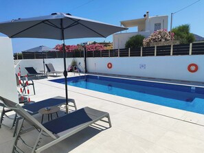 A swimming pool with lounge chairs and an umbrella, surrounded by a white wall with a lifebuoy and a sign. - Sunny & Blue 4 Luxury studio in beautiful Paros (Paros)