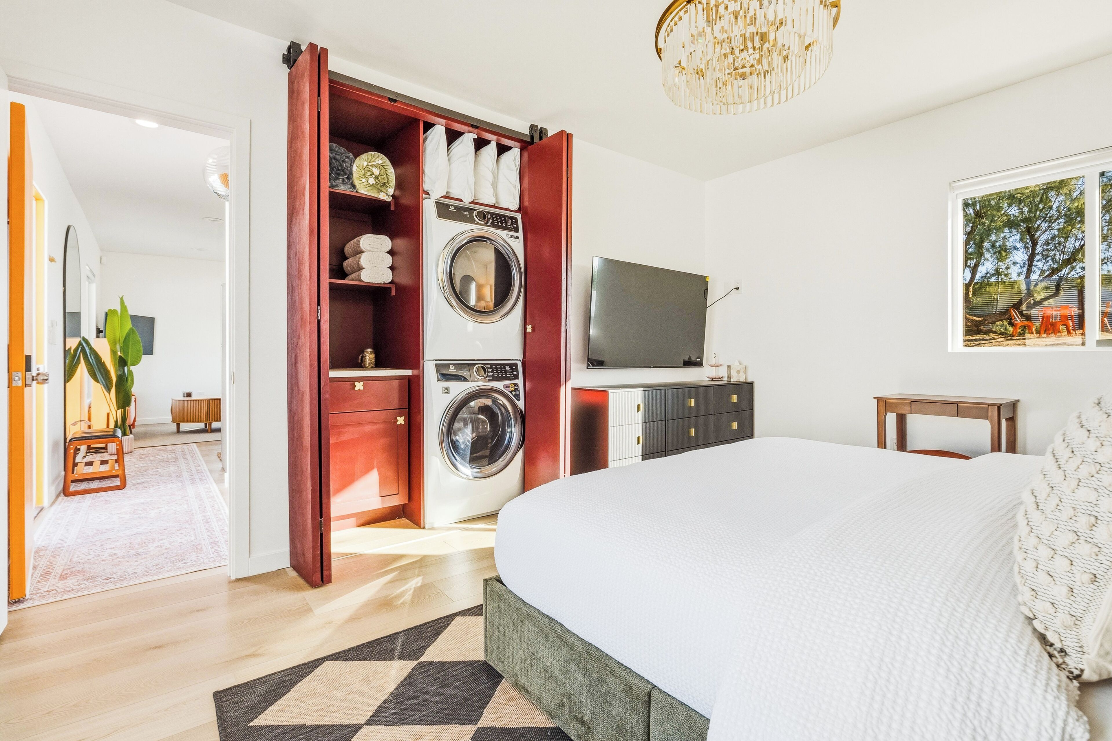 A bedroom with a bed, a washing machine, a television, and a window with a view.