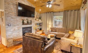 A living room with a fireplace, leather sofa, and a television mounted on the wall. - Sunny forest picnic w fire pit, CLEAN, UPDATED, 2-bedroom cabin, family-friendly (Overgaard)
