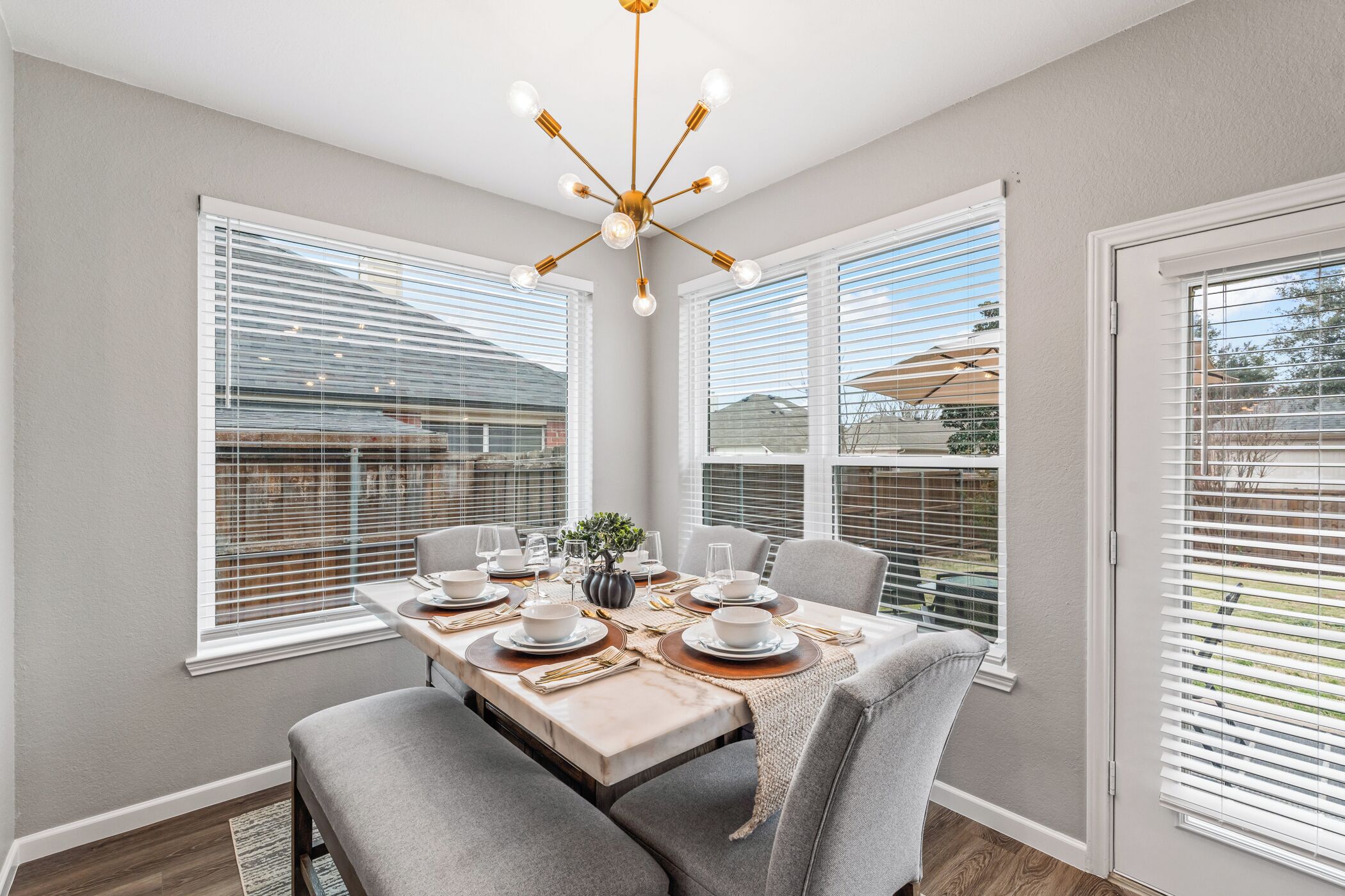 A dining room with a table set for six, large windows, and a modern chandelier.