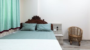 Ein Bett mit Holz Kopfteil, zwei Kissen, ein Nachttisch und ein Korbstuhl.