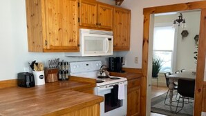 A kitchen with wooden cabinets, a microwave, a stove, and a dining area visible through an open doorway. - Green Mountain Retreat (Rutland)