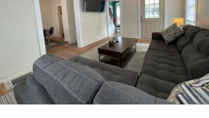 A living room with a sectional sofa, a coffee table, and a flat-screen TV mounted on the wall. - Green Mountain Retreat (Rutland)